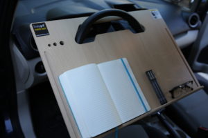 Contractor Wheeldesk mobile desk mounted on a car steering wheel with notebook, pens and glasses.